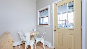 A small dining area with a round table and four white chairs, a beige couch, and a door with a window above it. - Cozy Studio w/ Full Kitchen (Hampton)