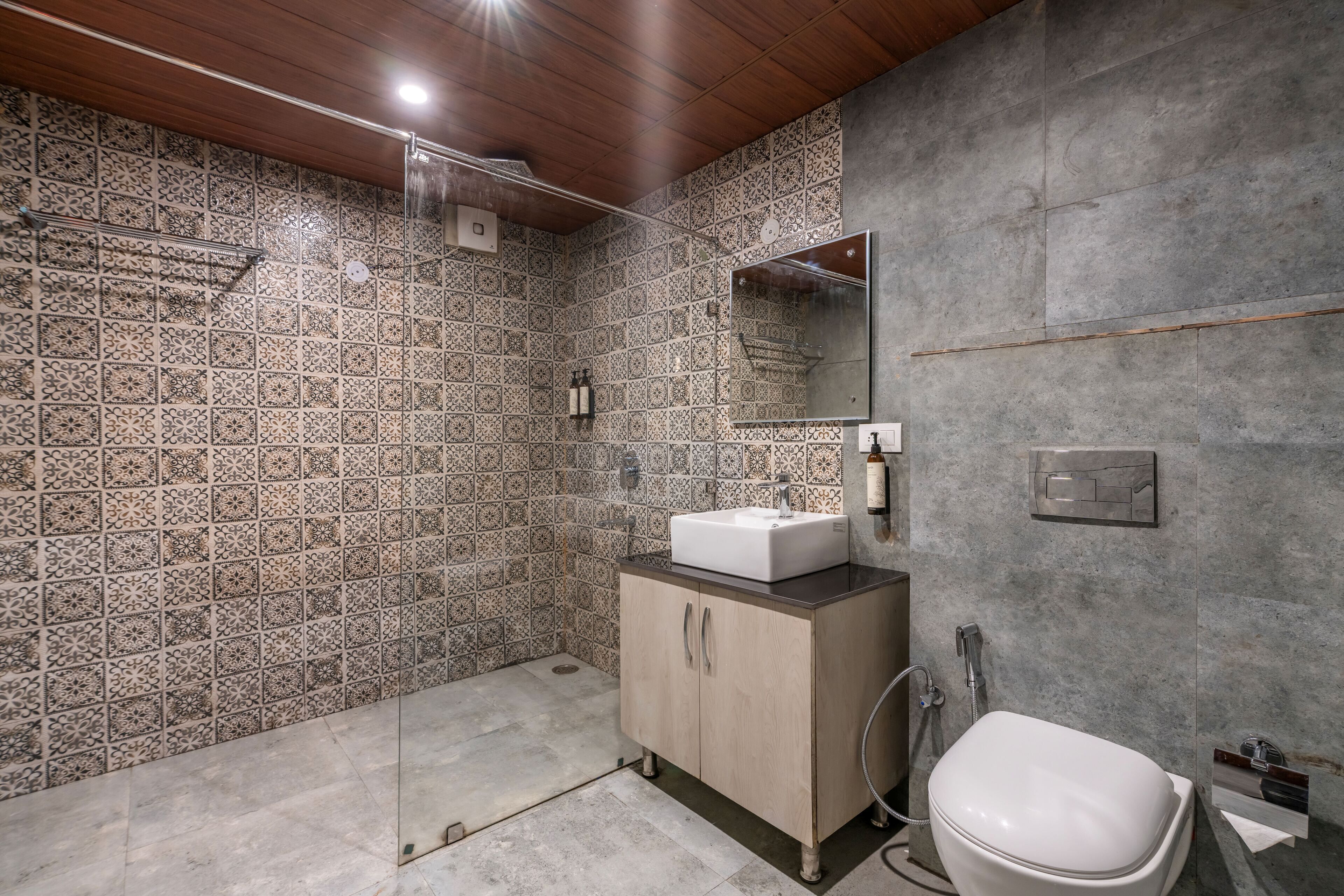Een moderne badkamer met patroontegels, een houten plafond, een glazen douchecabine, een wastafel en een toilet.