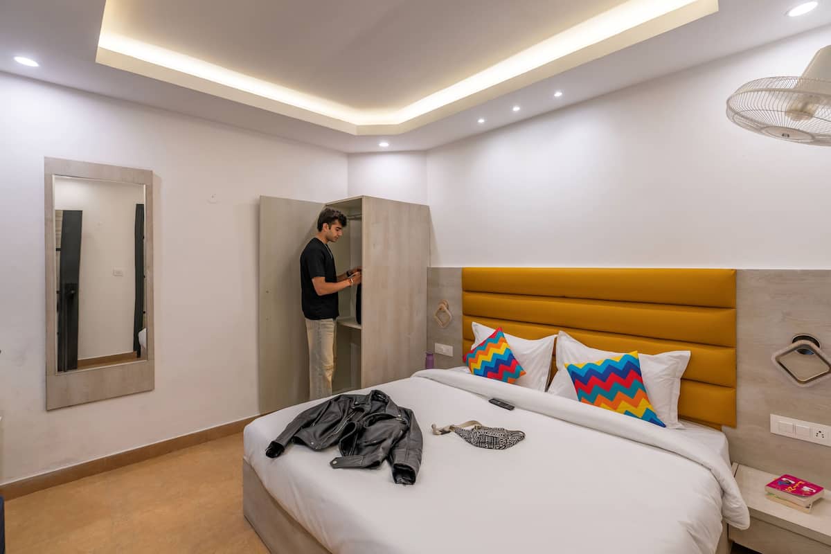 A modern hotel room with a bed, a wardrobe, a mirror, and a bedside table with a book.