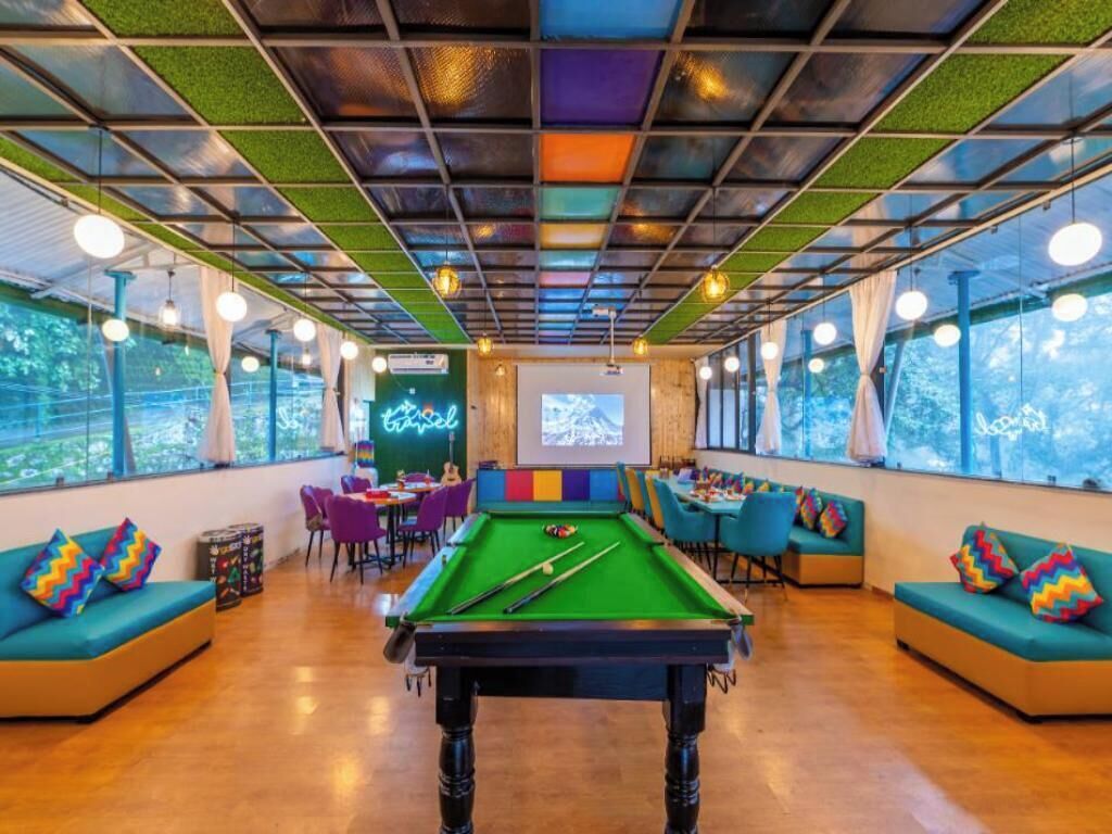 A pool table in a room with green cushions, a neon sign, and a projection screen.