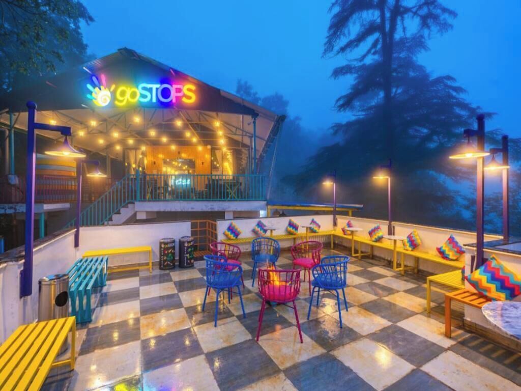 Un espace extérieur aménagé avec des chaises et des tables colorées, un sol à carreaux et un bâtiment sur lequel on peut voir une enseigne « goSTOPS ».