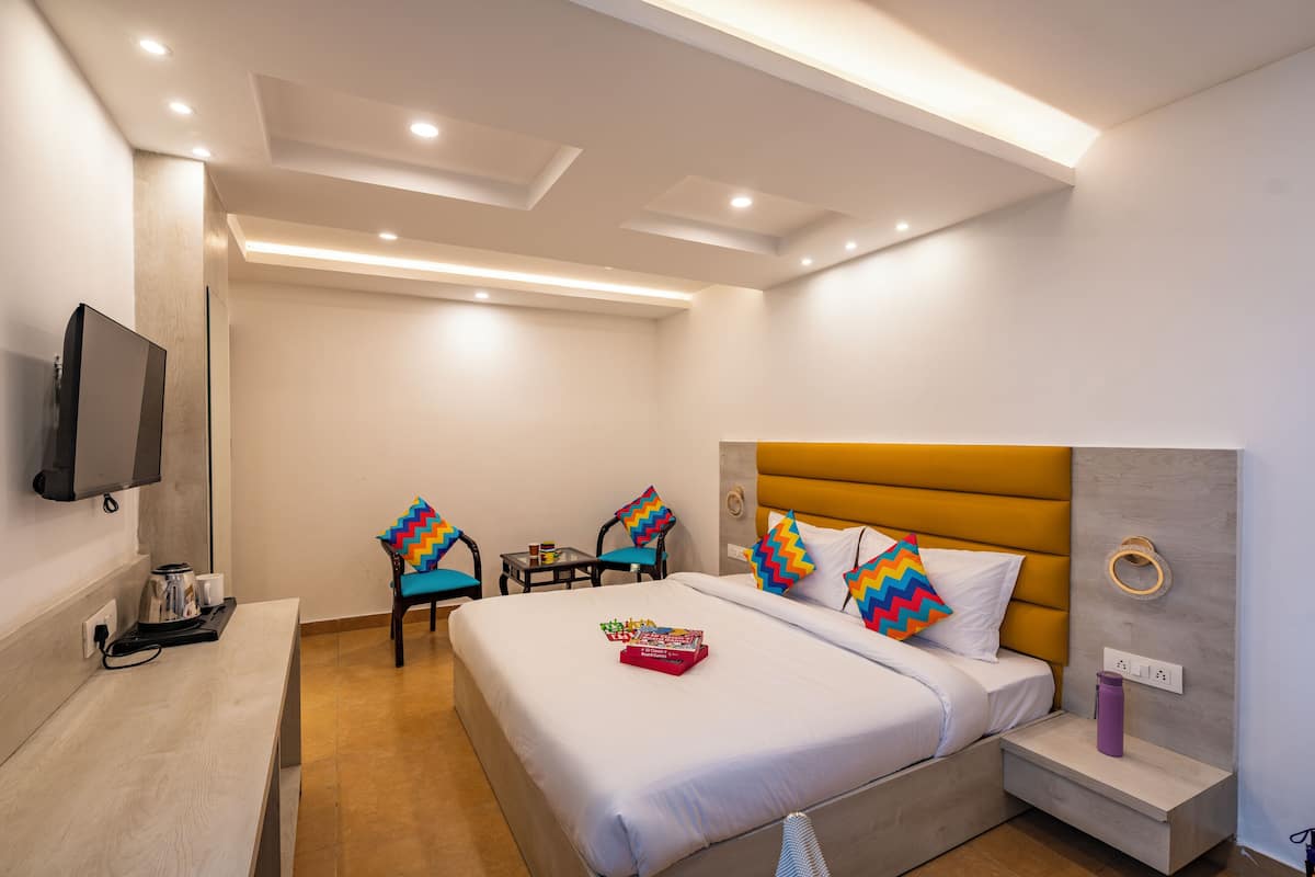 A modern hotel room with a bed, bedside table, TV, and a small seating area with chairs.