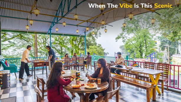 An outdoor dining area with tables and chairs, a checkered floor, and a view of trees and a building in the background. - goSTOPS Mussoorie Clock Tower (Mussoorie)