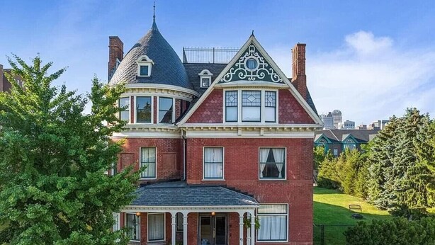 Una casa grande de dos pisos con una torre destacada y un porche que rodea toda la edificación.