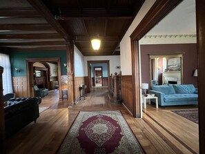 A hallway with wooden flooring, a patterned rug, a blue sofa, and a fireplace. - DC Whitney Mansion + Carriage House (Detroit)