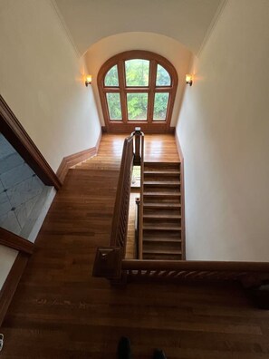 A wooden staircase leading to a loft bedroom with a large arched window overlooking a forest. - DC Whitney Mansion + Carriage House (Detroit)