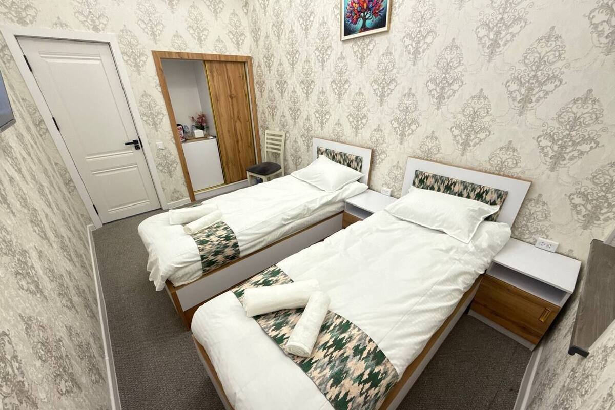 A hotel room with two single beds, a wooden wardrobe, a mirror, and a small bedside table.