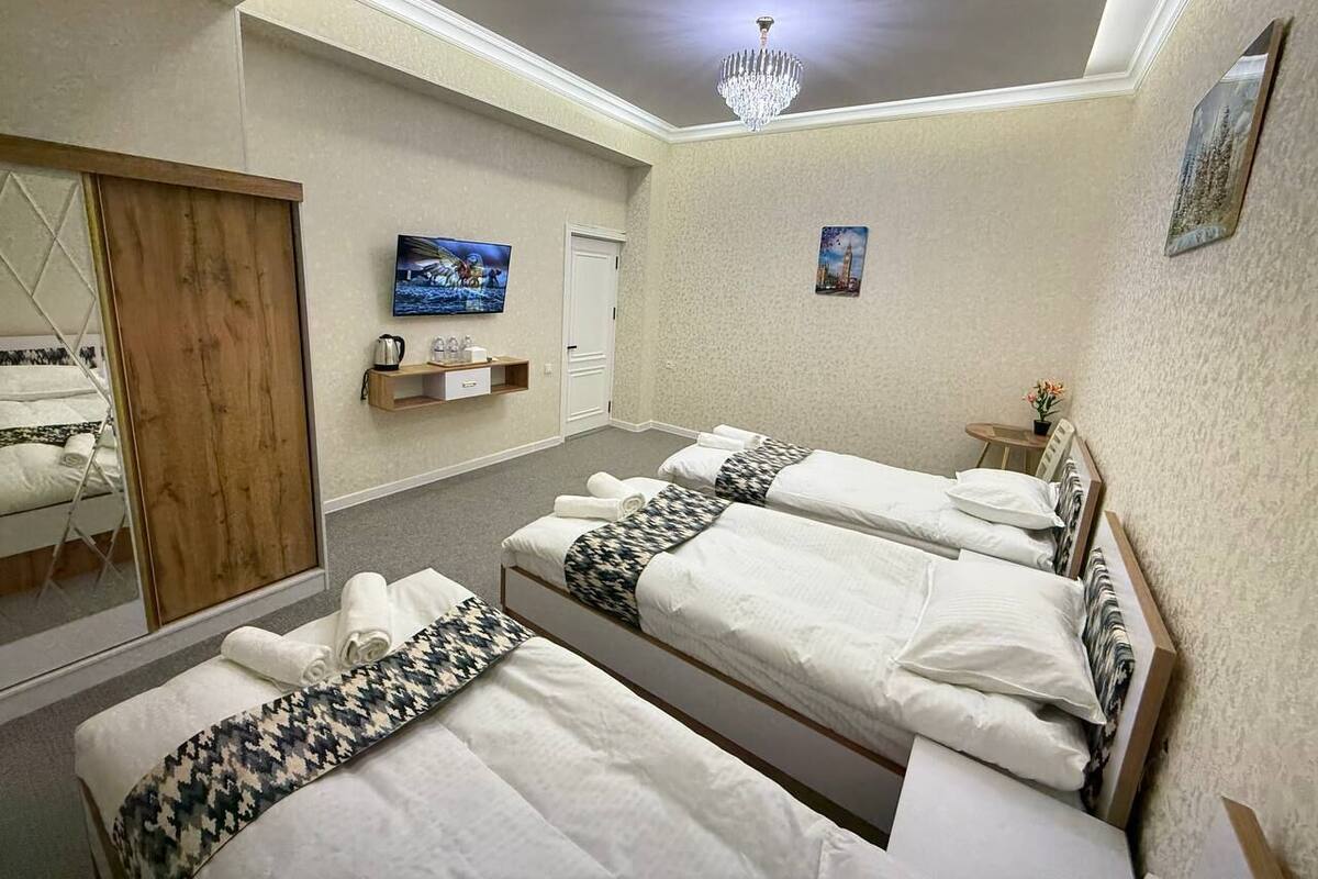 A hotel room with three beds, a wooden wardrobe, a mirror, a chandelier, and artwork on the walls.