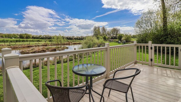 A deck with a table and chairs overlooking a pond and greenery. - The Dragonfly (Driffield)