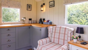A cozy kitchen with a wooden countertop, grey cabinets, a plaid armchair, and a window with a view of greenery. - The Dragonfly (Driffield)