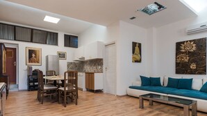 Ein geräumiger Wohnbereich mit einer Couch, einem Couchtisch und einem Esstisch. Es gibt eine Küchenzeile mit Schränken und einem Kühlschrank.
