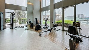 A spacious gym with various exercise equipment, large windows, and a view of the cityscape. - Elegant 1 Bed | Canal Views | Close to Ain Dubai I 5242 Tower 2 (Dubai Marina)