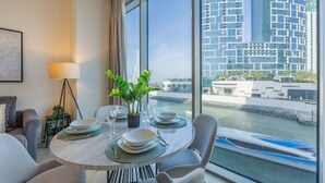 A dining area with a table set for four, a potted plant, and a view of a modern building and water body. - Elegant 1 Bed | Canal Views | Close to Ain Dubai I 5242 Tower 2 (Dubai Marina)