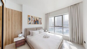 A modern hotel room with a large bed, a nightstand, a painting on the wall, and a view of the city through the window.
