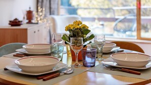 A dining table set with plates, bowls, glasses, and cutlery, with a vase of yellow flowers in the center.