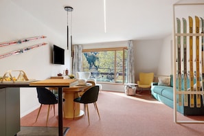 A modern living room with a dining area, a TV mounted on the wall, and a ski rack.