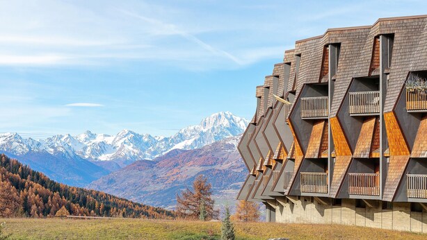 A modern building with a unique geometric design, large balconies, and a mountainous backdrop.
