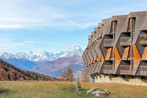 A modern building with a unique geometric design, large balconies, and a mountainous backdrop.