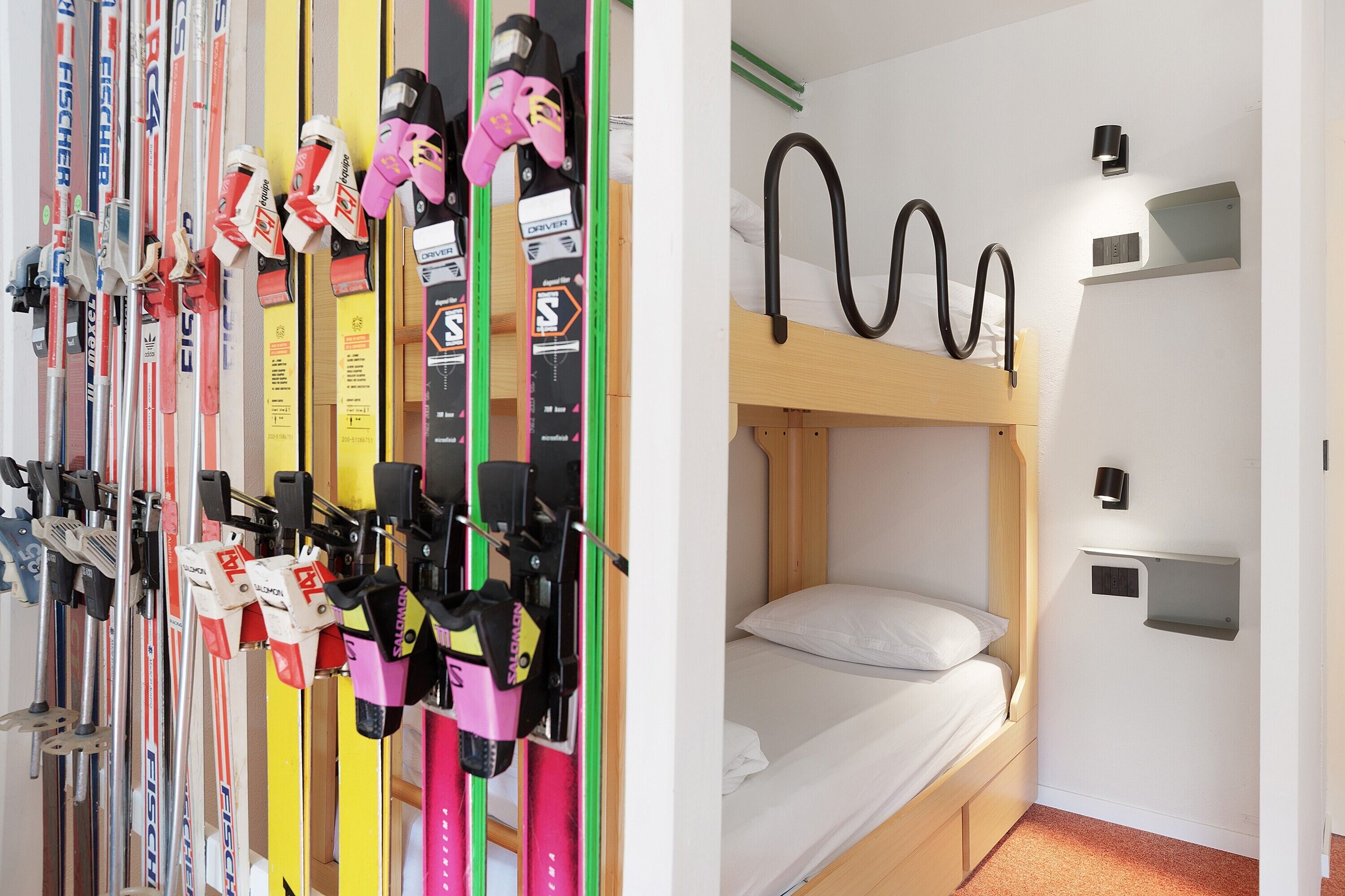 Un lit superposé avec un matelas et des oreillers, un luminaire fixé au mur et une étagère.