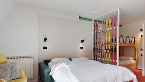 A modern hotel room with a bed, a seating area with a chair and sofa, a ski rack, and a bunk bed.