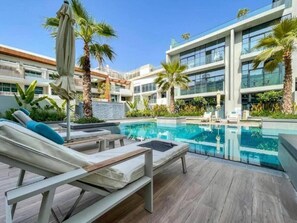A modern hotel with a pool area, lounge chairs, and palm trees. - Vibrant Studio l Peaceful Retreat l Heart of JVC (Jumeirah Village Circle)