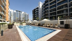 A rooftop pool with lounge chairs and umbrellas, surrounded by modern buildings.
