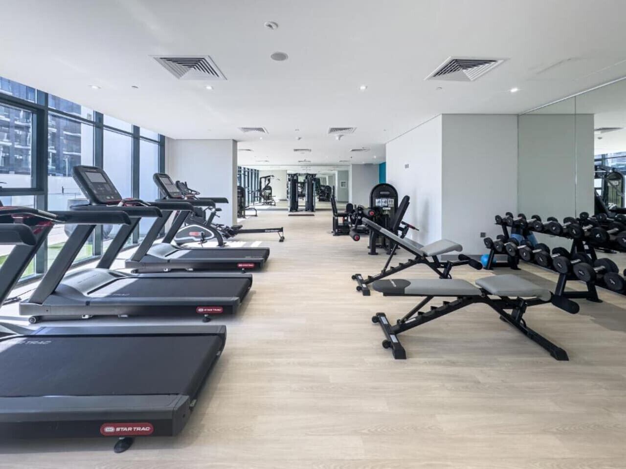Une salle de sport moderne équipée de tapis de course, de bancs de musculation et d’haltères.