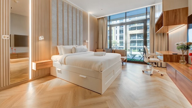 A modern hotel room with a large bed, a desk, and a view of the city through large windows.