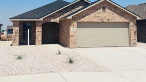 A single-story brick house with a garage, a clear sky, and a gravel driveway. - New construction 3-bedroom house in beautiful Midland with 2 car garage access. (Midland)