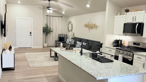 A modern kitchen with a central island, white cabinetry, stainless steel appliances, and a ceiling fan. - New construction 3-bedroom house in beautiful Midland with 2 car garage access. (Midland)