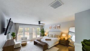 Un dormitorio moderno con cama, mesitas de noche, televisor y puerta corrediza de vidrio que da a un espacio exterior.