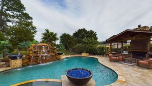 Una piscina con cascada, un jacuzzi y mobiliario de exterior.