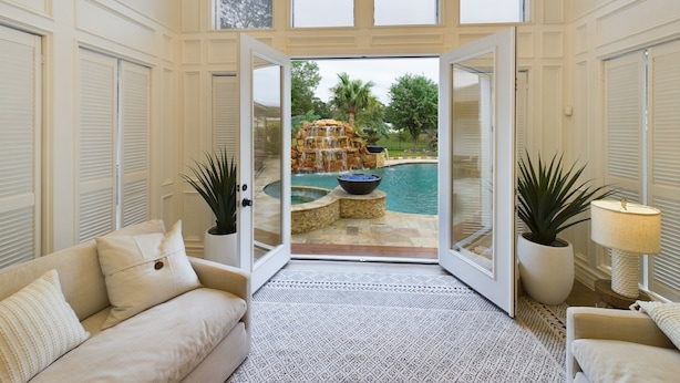 Amplia habitación con un gran ventanal corredero que da a un patio trasero con piscina y una cascada.