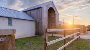 A rustic barn with a metal roof and a wooden door, adjacent to a white building with a window. - The Little Stable - Cosy 1 Bed Cottage in Burford (Burford)