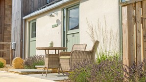 A building with a green door, a small outdoor table with chairs, and lavender plants. - The Little Stable - Cosy 1 Bed Cottage in Burford (Burford)
