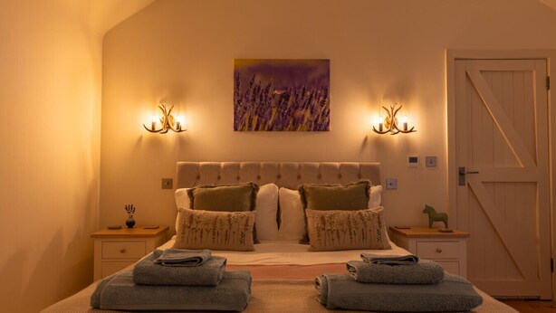 A bedroom with a large bed, two bedside tables, a door, and a painting on the wall. - The Little Stable - Cosy 1 Bed Cottage in Burford (Burford)