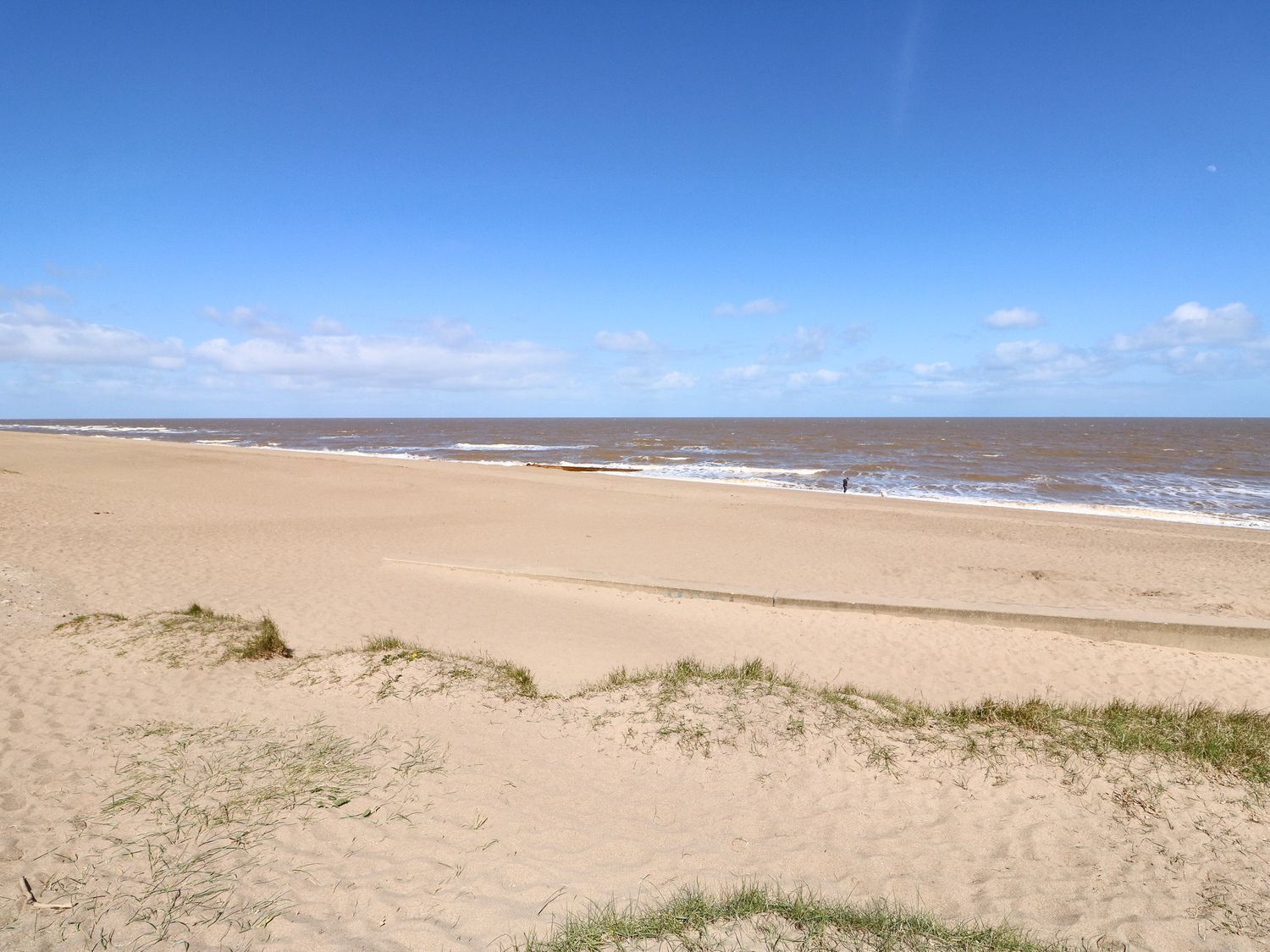 A wide sandy beach with gentle waves and a clear sky.