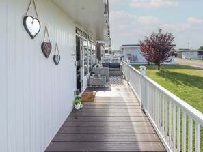 A covered porch with a wooden deck, white railings, and a seating area with wicker furniture. - 3 Cherry Blossom (Skegness)
