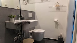 A modern bathroom with a glass partition, a sink, a toilet, and a small round stool. - Arbio I Duxen Apartments Hagenbeck Zoo (Hamburg)