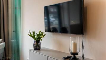 A modern living room with a flat-screen TV mounted on the wall, a small cabinet with a potted plant, and a candle holder.