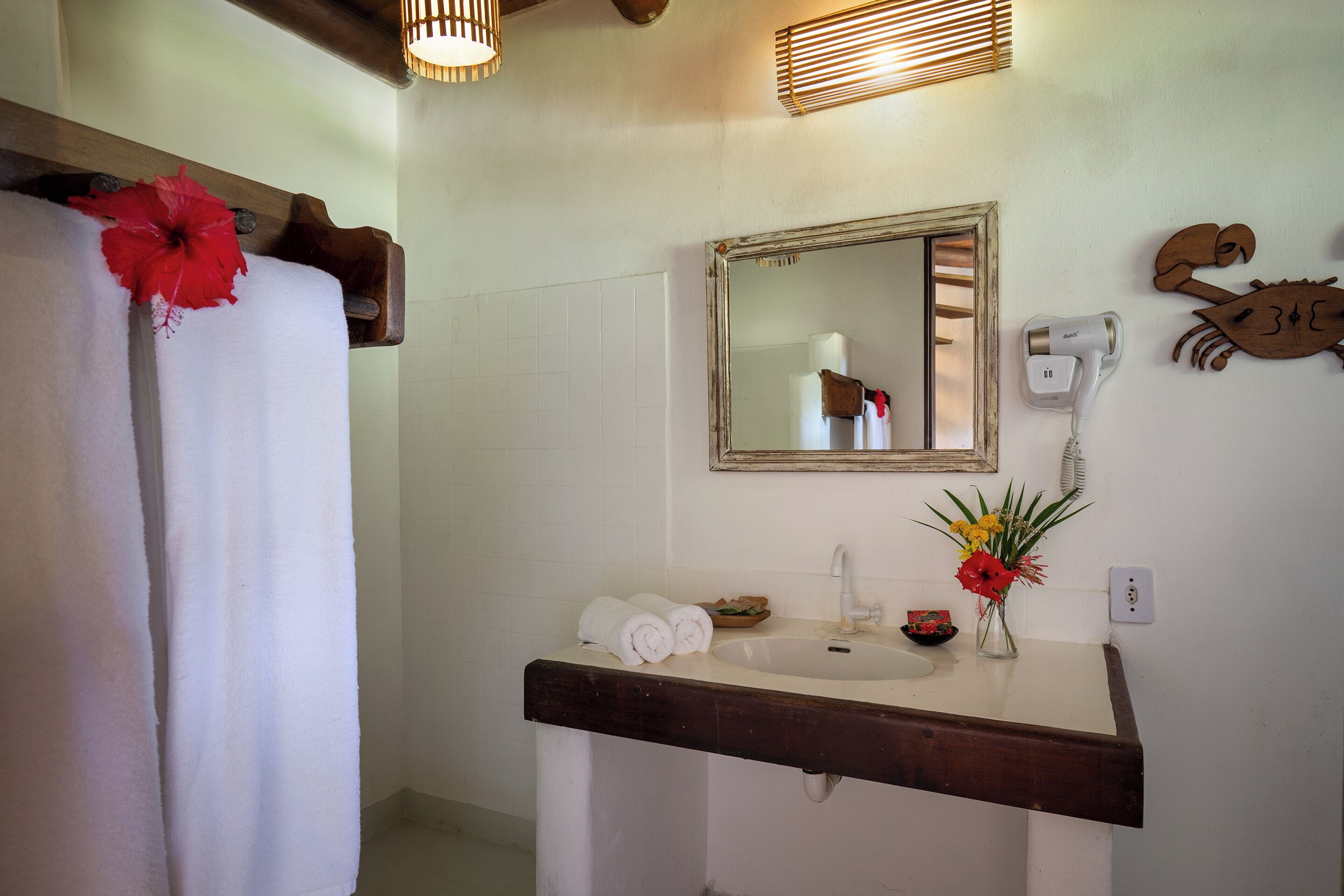 A bathroom with a white sink, a mirror, a towel rack, a hairdryer, and a decorative crab wall piece.