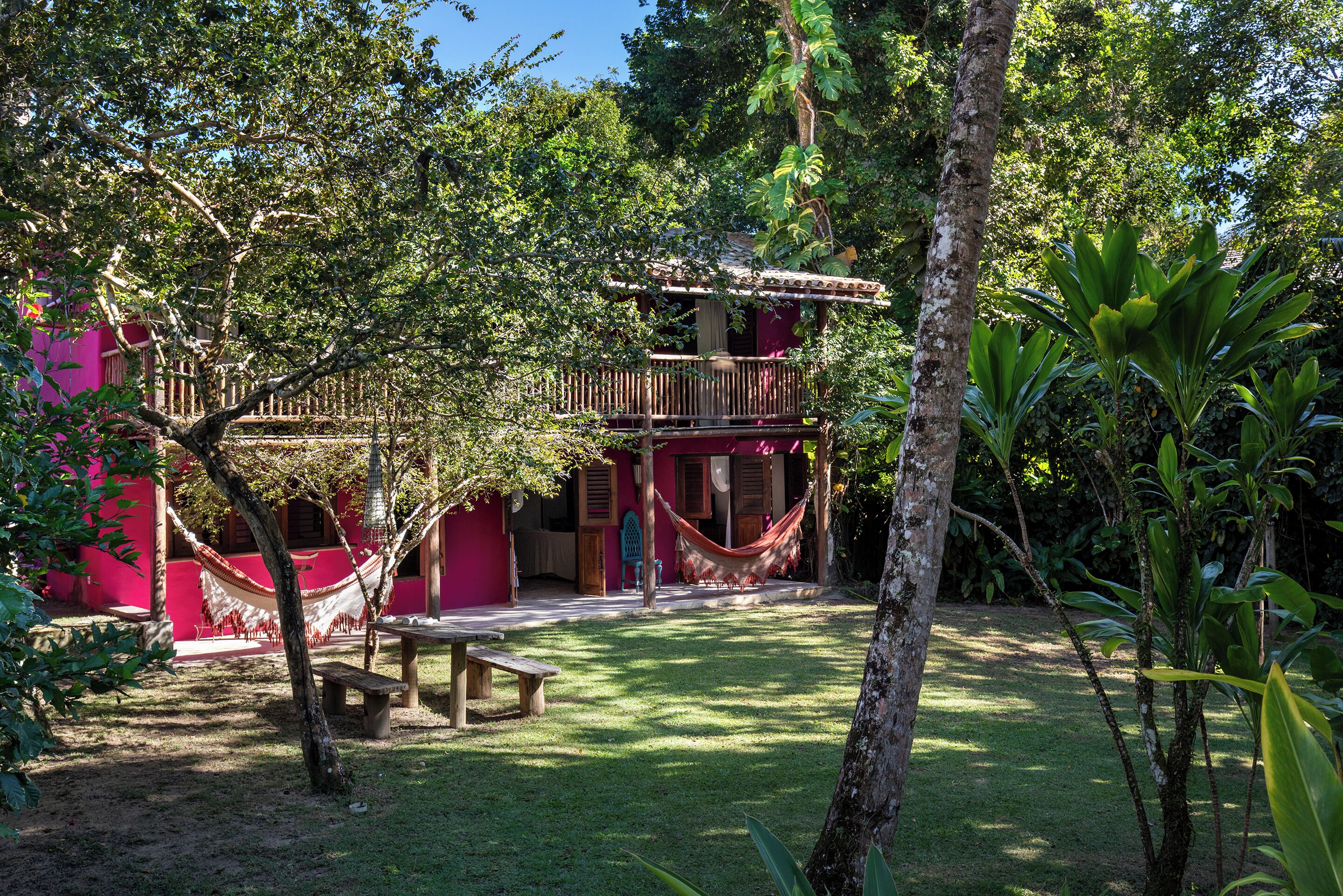 Uma casinha na árvore com rede, um banco e uma pequena mesa em um jardim exuberante.