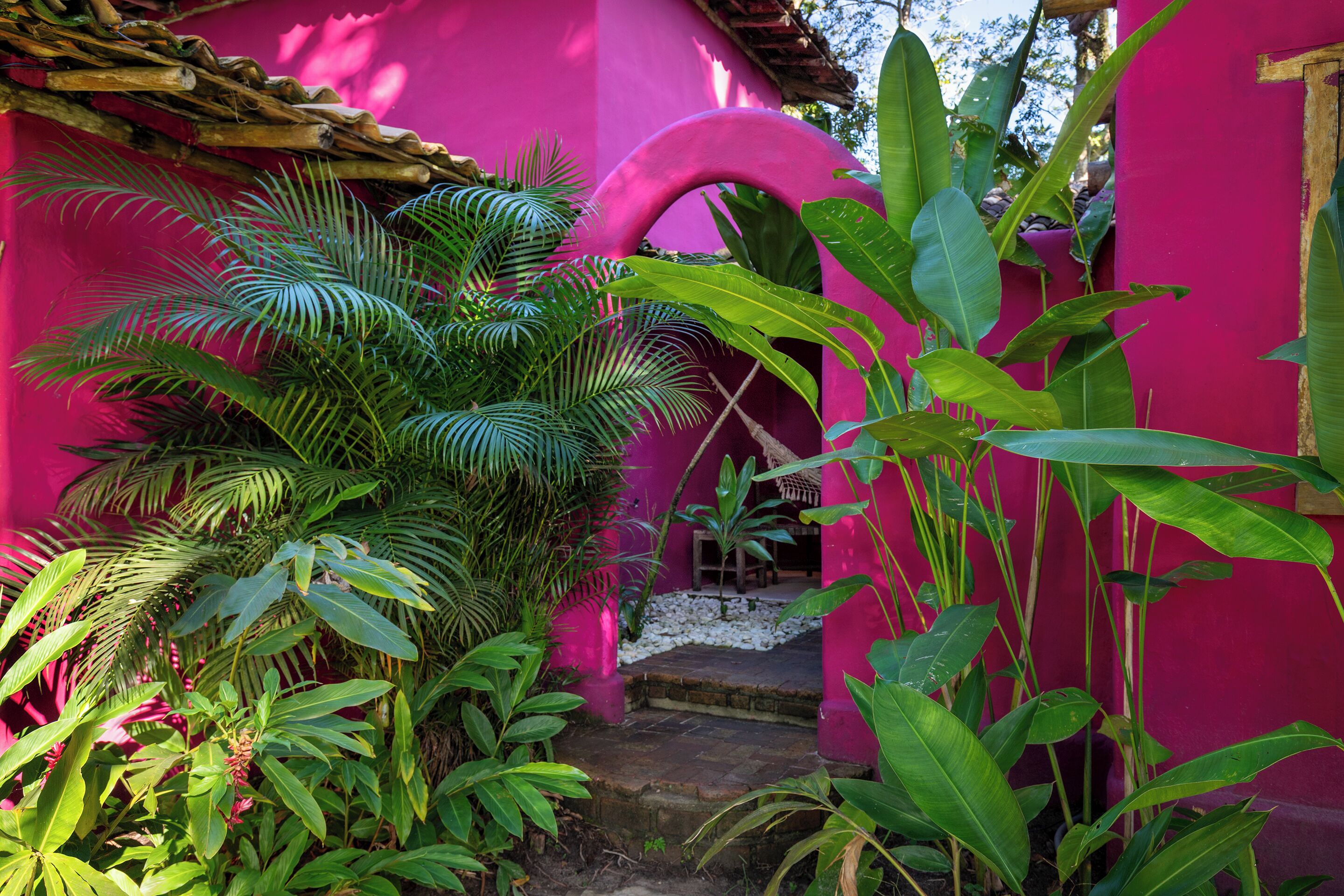 A pink building with a wooden roof, surrounded by lush green foliage.