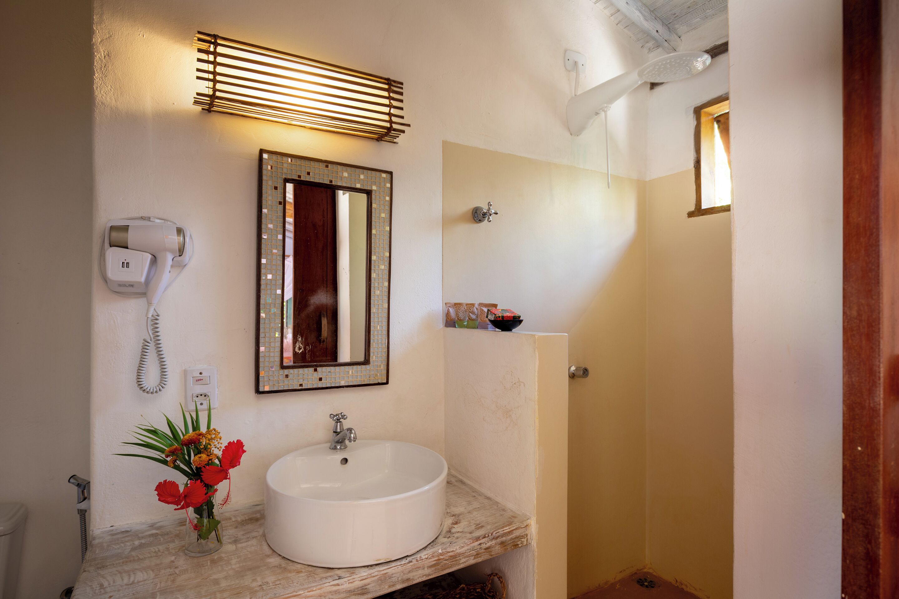 Une salle de bain équipée d’un lavabo, d’un miroir, d’un sèche-cheveux et d’une petite fenêtre.