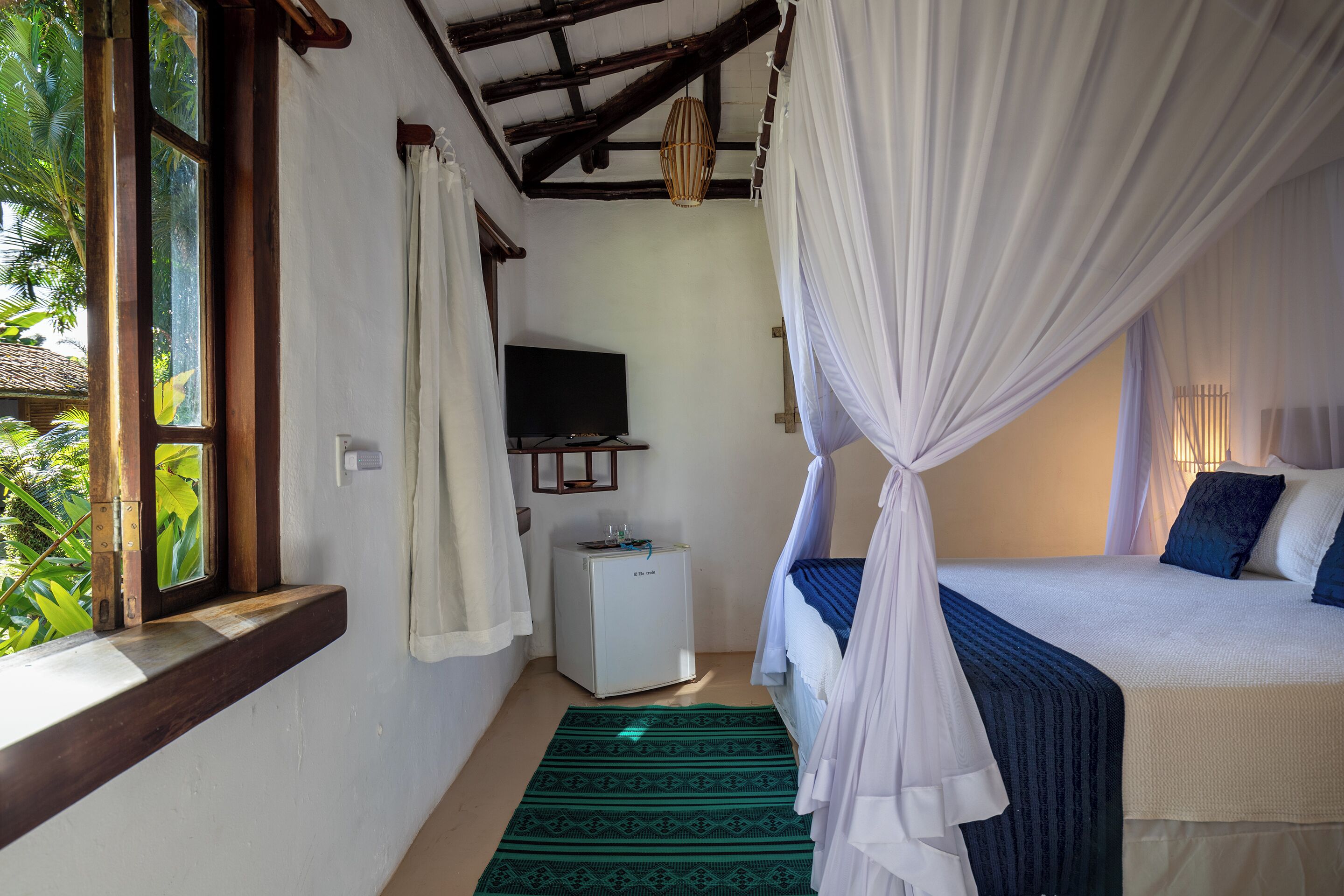 A bedroom with a bed, a television, a small white cabinet, and a window with curtains.