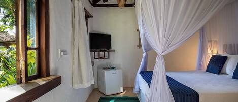 Un dormitorio con una cama, televisor, un pequeño armario blanco y una ventana con cortinas.