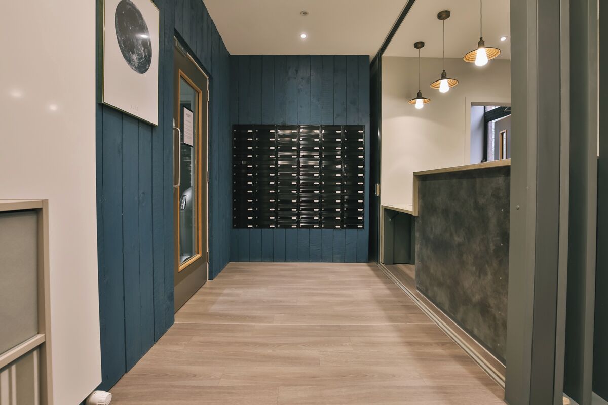 Un pasillo con piso de madera, pared azul y un separador negro con varios ventanales pequeños.