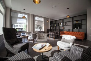 A modern living room with a sofa, armchairs, and a coffee table. There are bookshelves and a large window providing natural light. - Student Only Bath Street (Glasgow)
