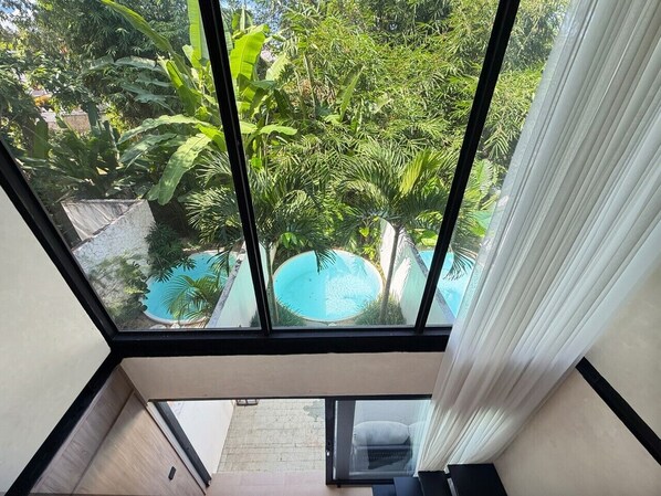 Une chambre avec vue sur une piscine, entourée d’une végétation luxuriante.