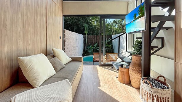 A modern living room with a wooden floor, a sofa with cushions, a coffee table, and a TV mounted on the wall. - Luxury Private Pool Loft Canggu (Canggu)